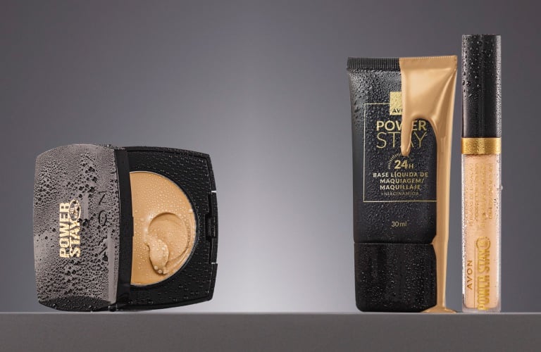 Uma base compacta e outra líquida da Power Stay ao lado de um corretivo lacrado da Avon em tons claros, ilustrando se o corretivo é antes ou depois da base.